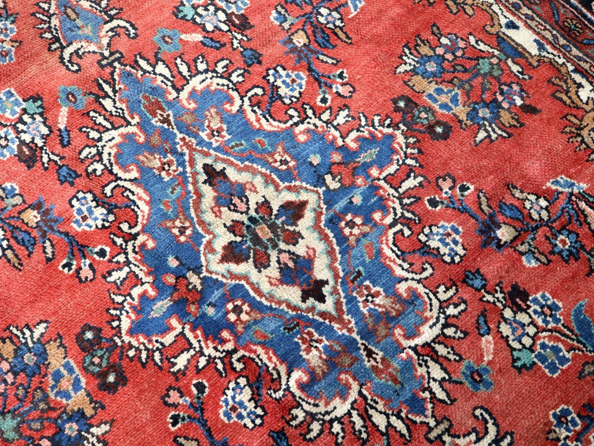 Persian rug close-up: rust red background with blue and cream curling vine motifs