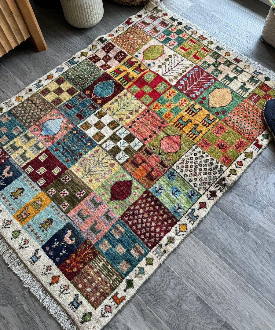 Multicolor Persian Gabbeh rug with geometric patchwork design and fringed edges on light background