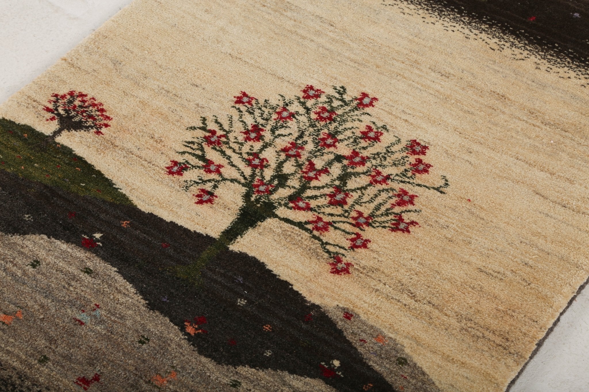 Close-up of Persian Gabbeh rug corner with red tree motif on cream and dark banding