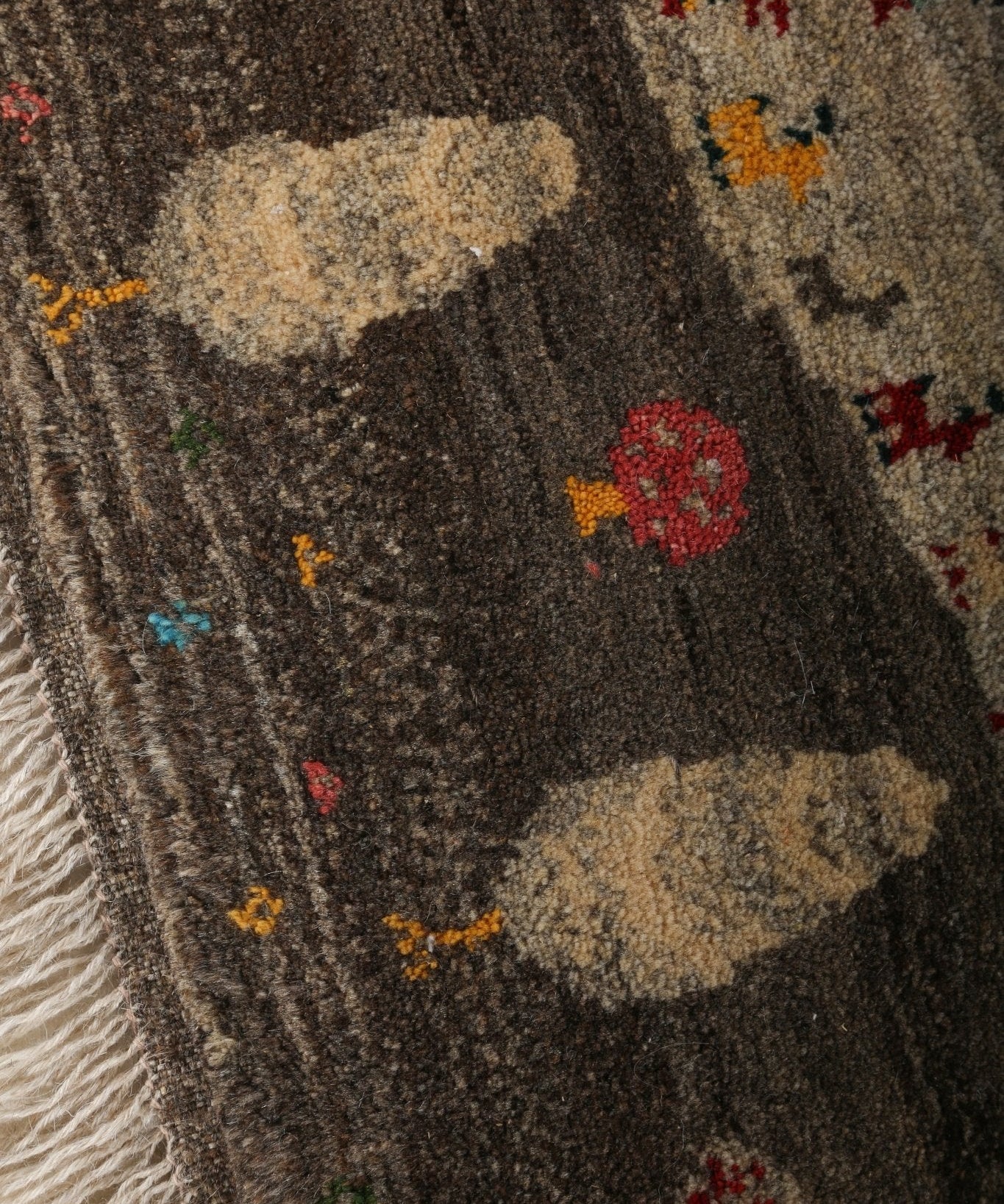 Gabbeh rug close-up detail with dark ground, cream shapes, and colorful tiny scattered motifs