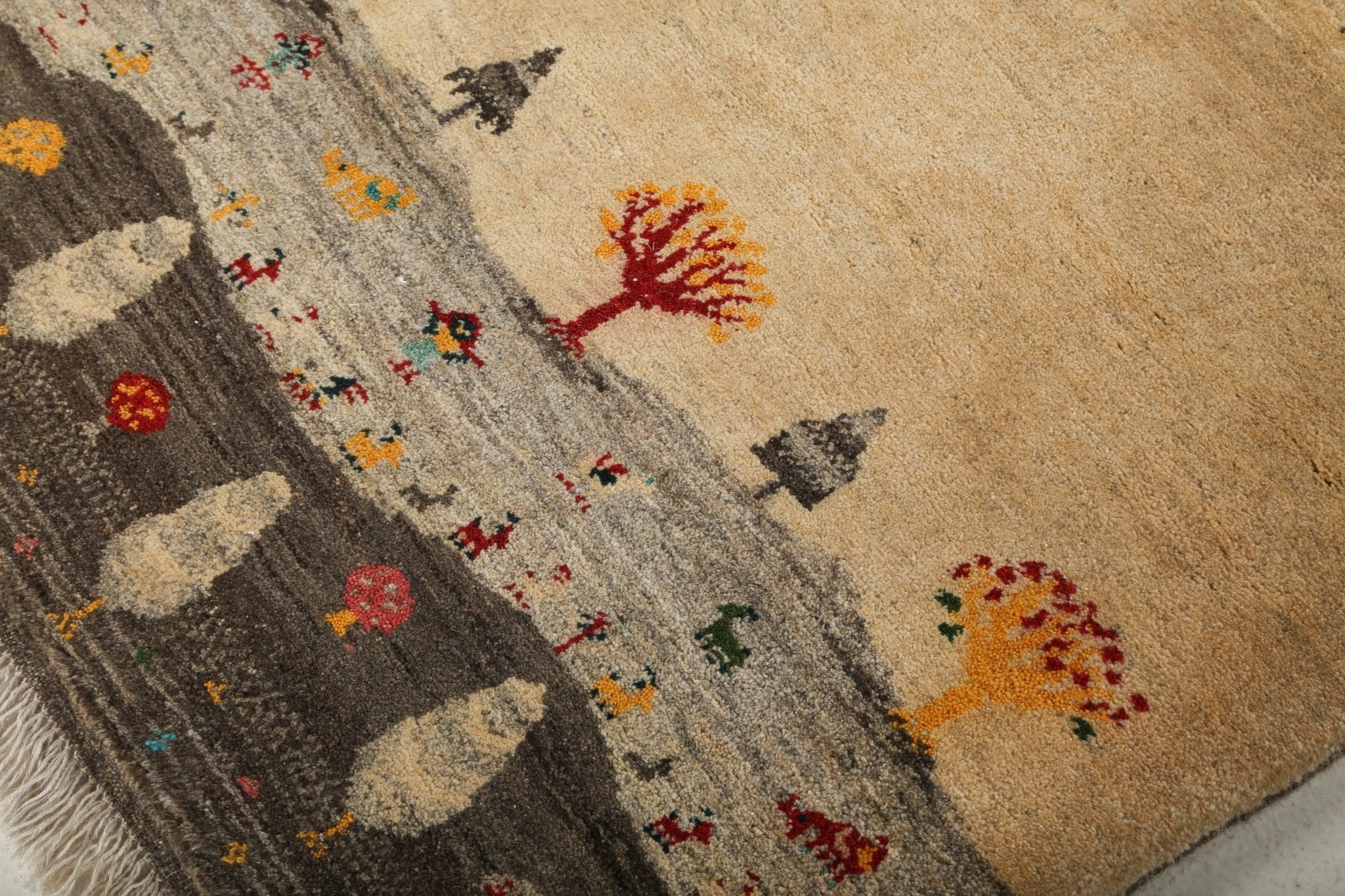 Gabbeh rug detail close-up with beige background, colorful trees, and small animal figures