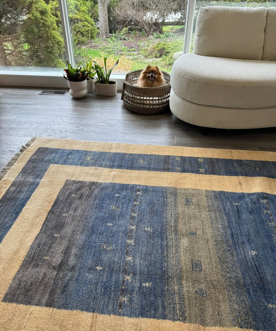 Large gabbeh-style rug with blue-gray field, beige framing stripes, short fringed ends