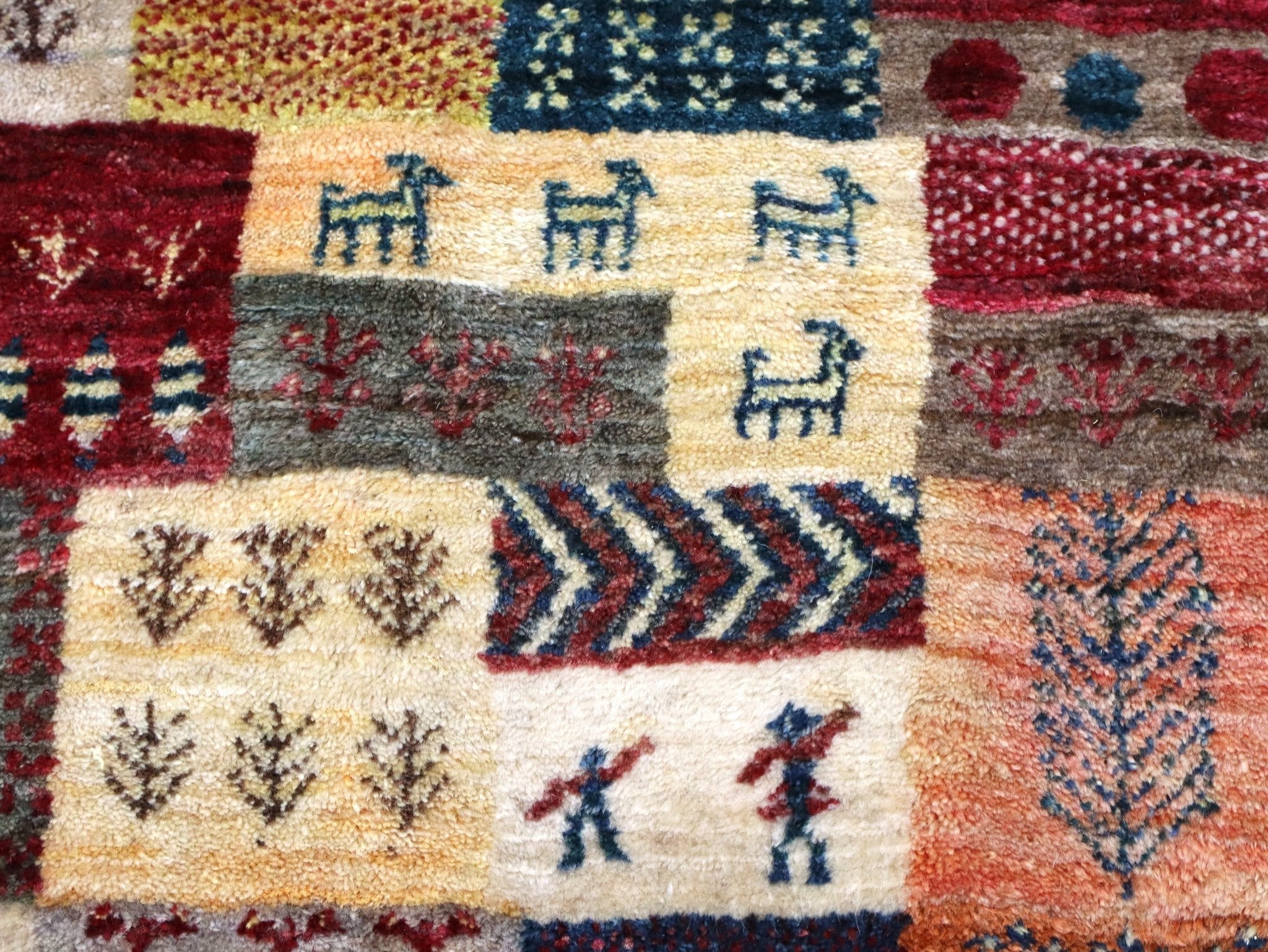 Persian Gabbeh-style rug close-up with red, blue, and cream motifs and zigzag band