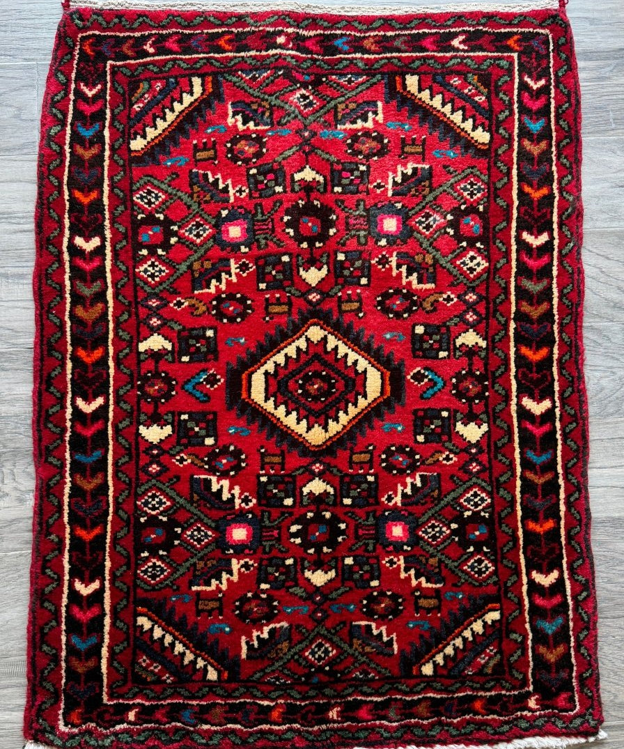 Red Persian-style rug with central diamond medallion, geometric border, and fringed edges.
