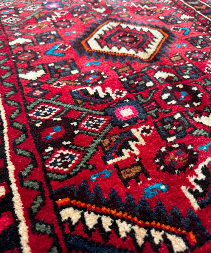 Red and dark navy rug section with central medallion and small geometric motifs.