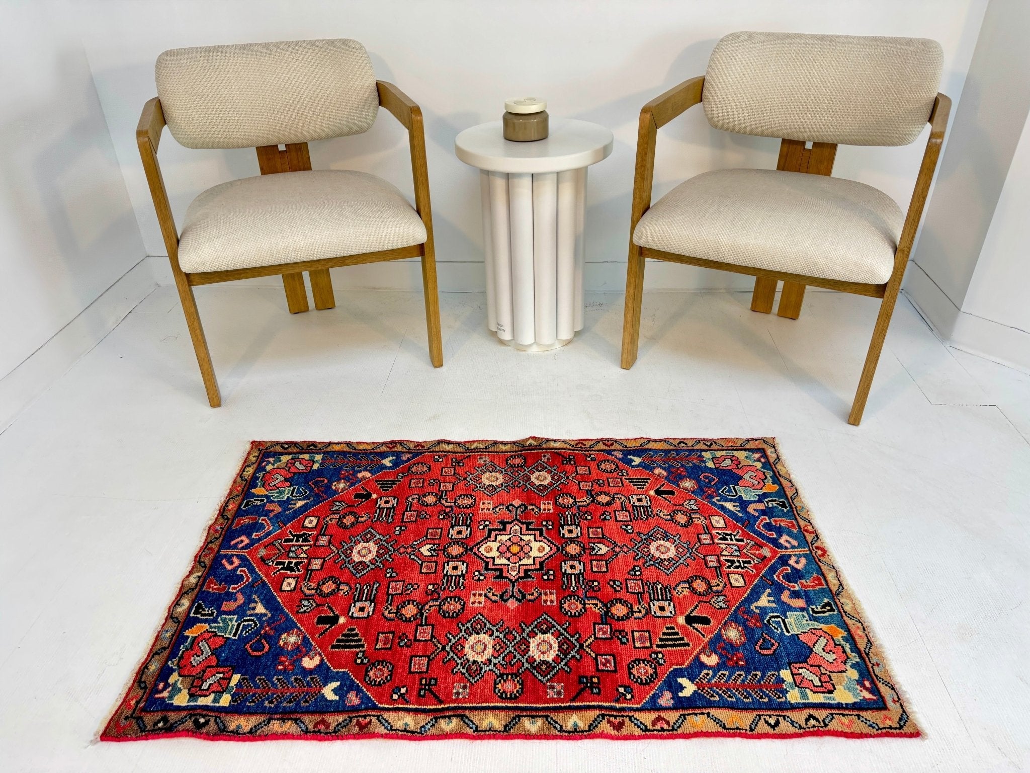 Persian Hamadan rug on white floor with red field and blue geometric border.