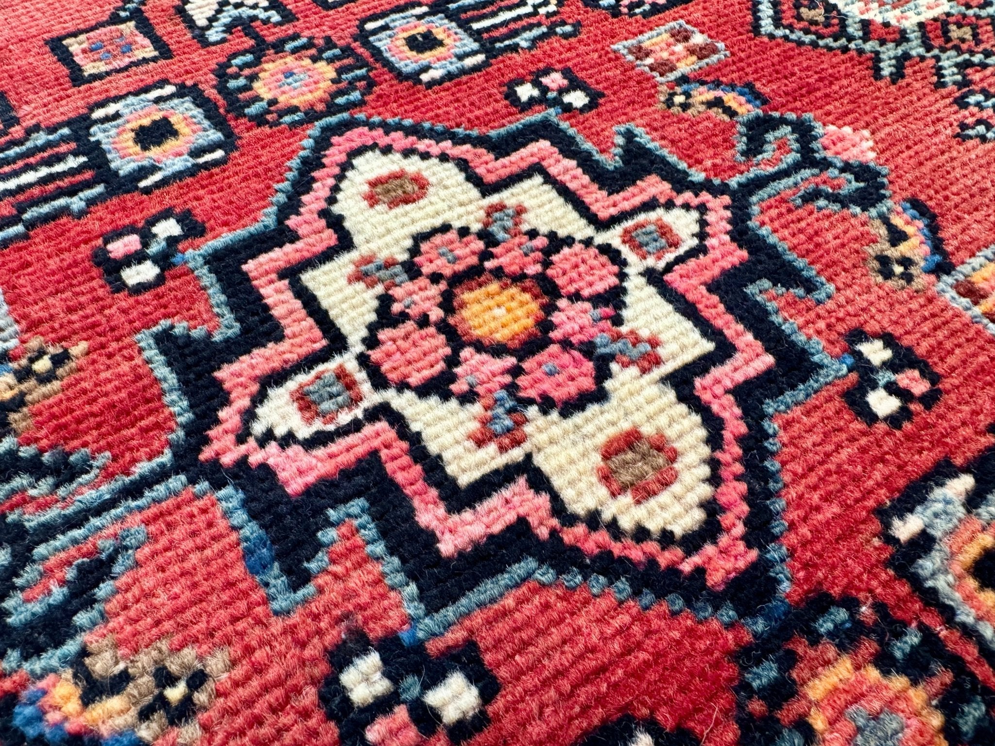 Red Persian rug with central medallion, navy outlines, and small multicolor motifs.
