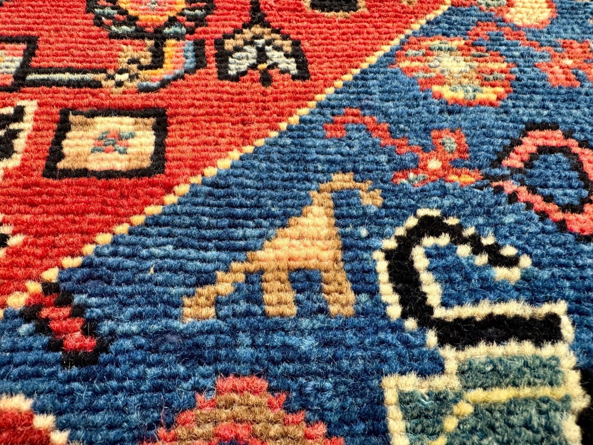 Close-up of blue and red rug pile with multicolor geometric pattern and texture.