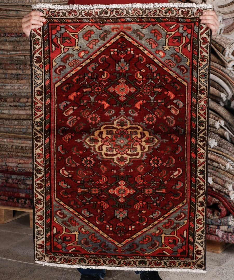 Red Persian-style area rug held up, featuring cream medallion and ornate geometric border.