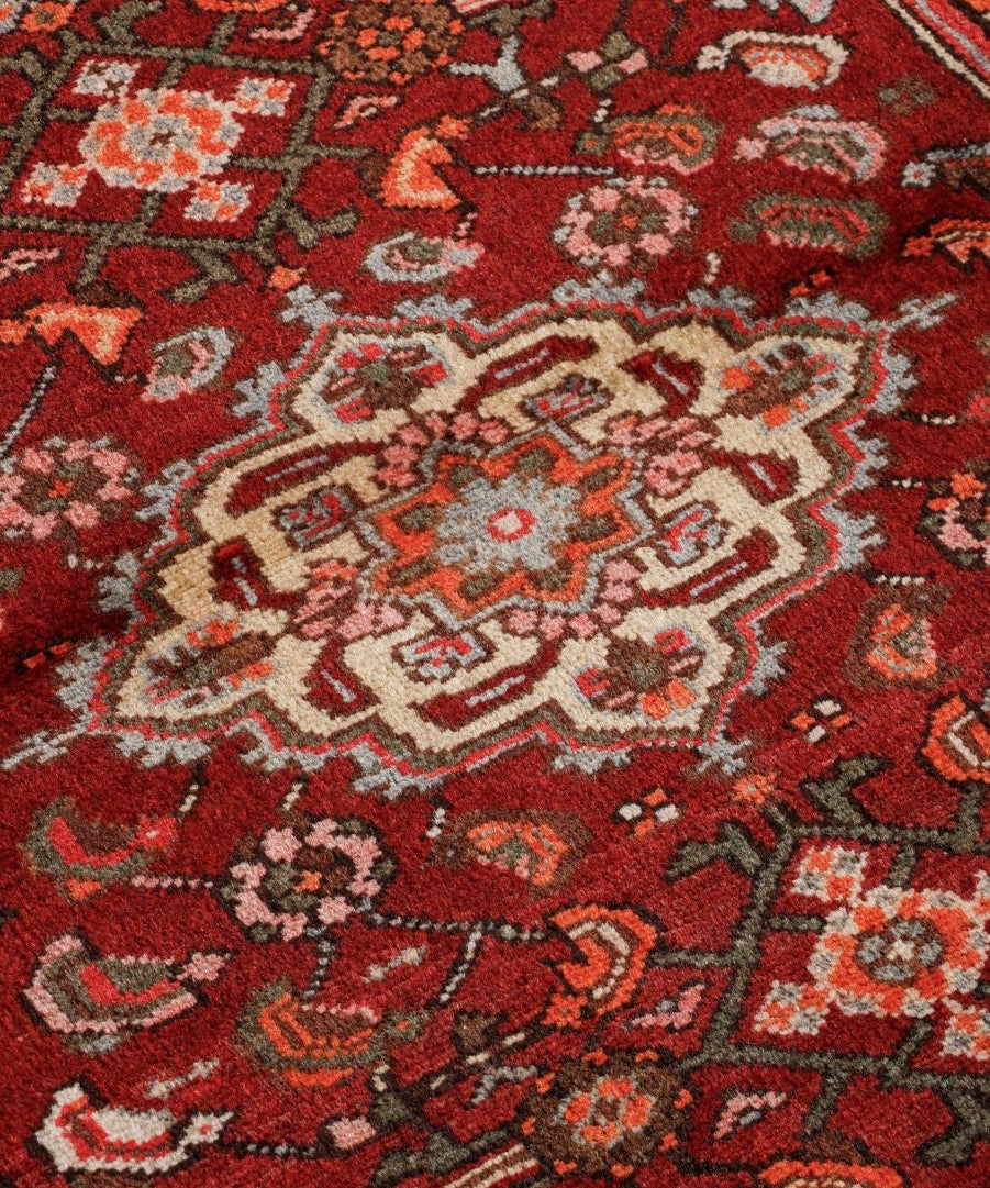 Close-up of red rug with cream floral and geometric motifs and dark outlining.
