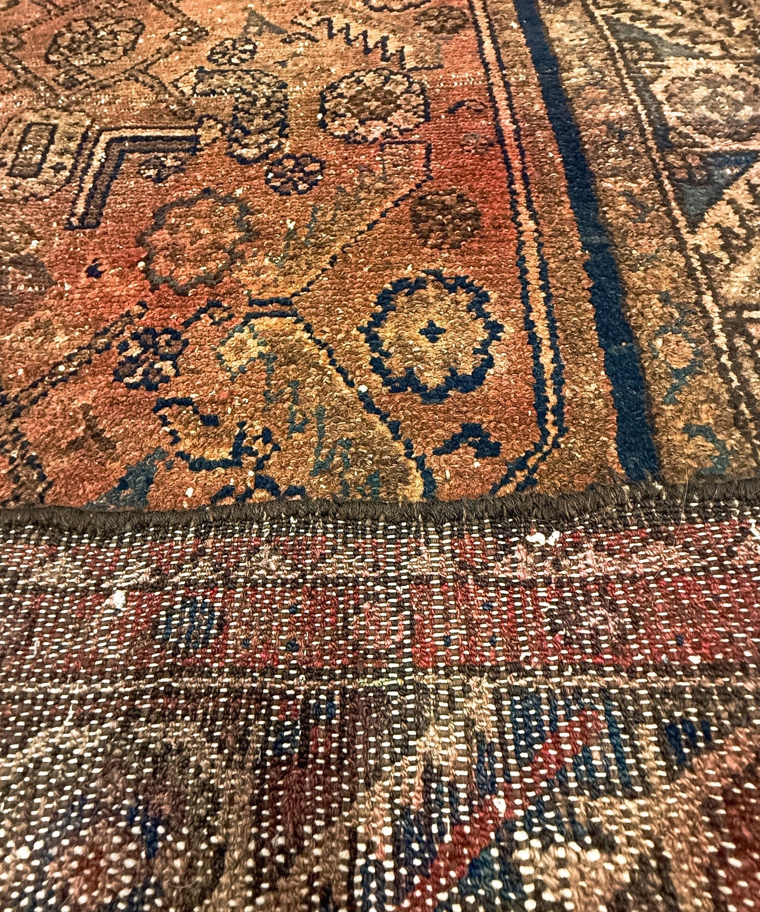 Rug close-up with rust-brown, navy, and gold floral-geometric motifs and fringe edge