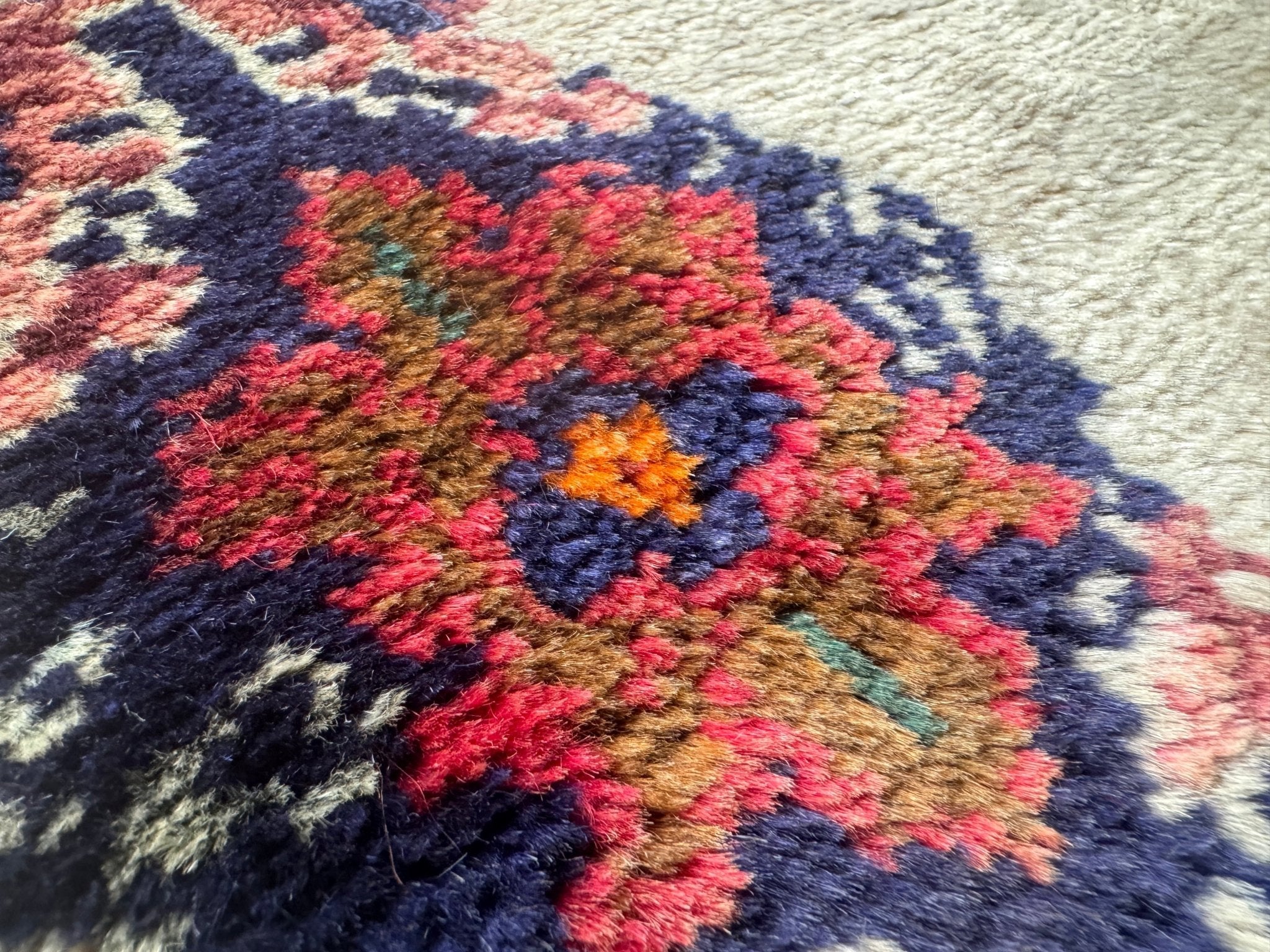 Persian Hamadan-style rug close-up showing navy and red rosette motifs on cream ground.