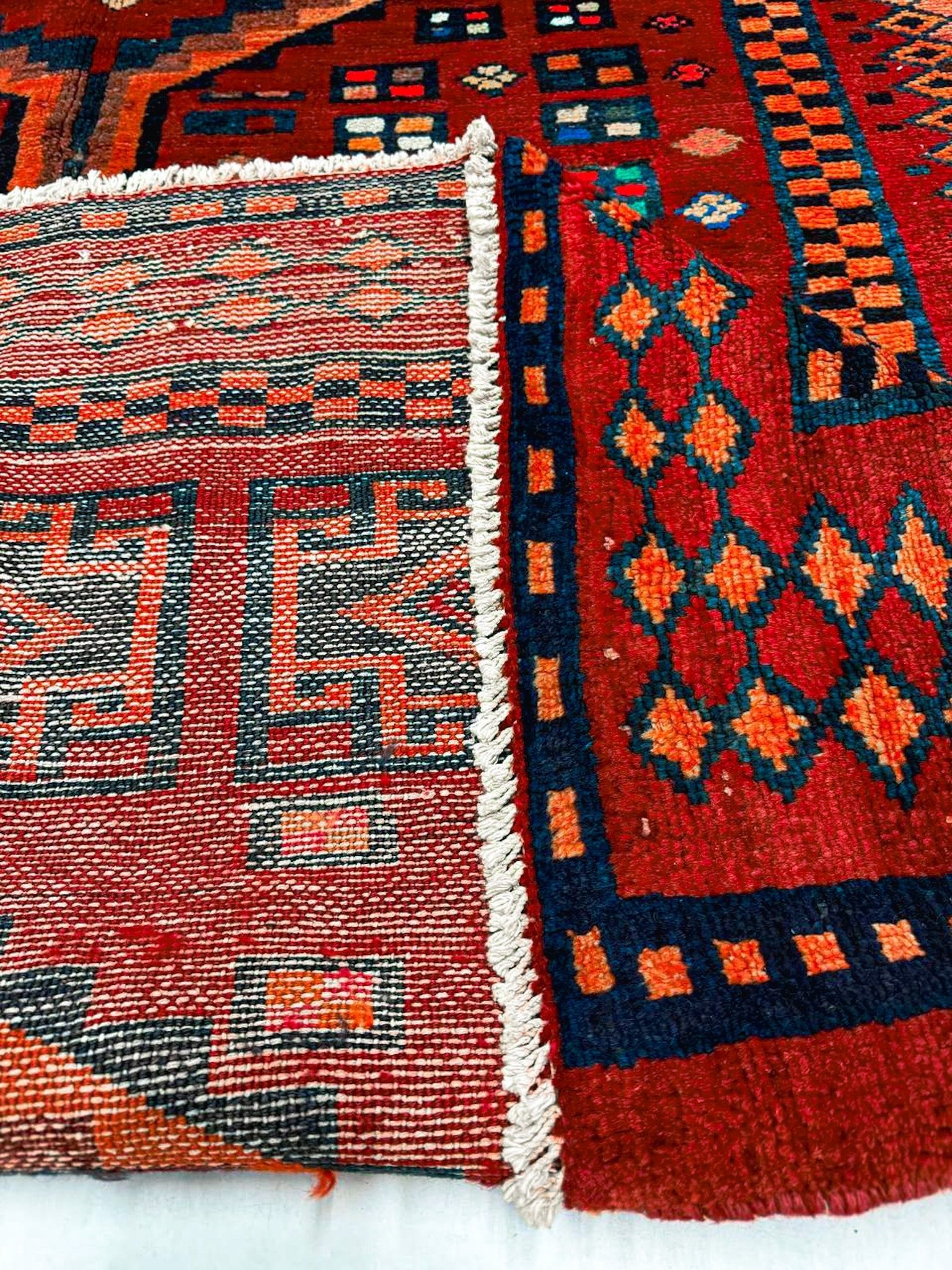 Close-up of rug fringe and side design: white band border with navy and red motifs.