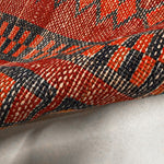 Close-up of red rug border with navy and orange geometric lines and textured woven pile.