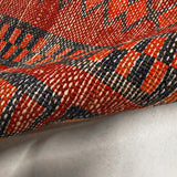 Close-up of red rug border with navy and orange geometric lines and textured woven pile.