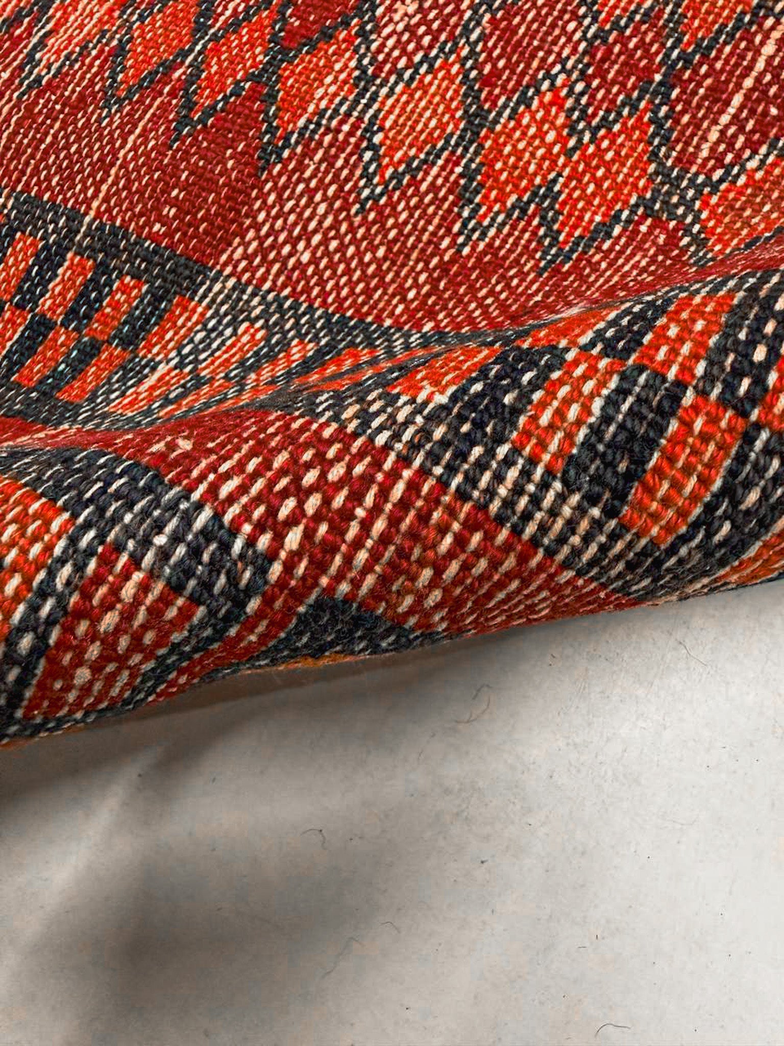 Close-up of red rug border with navy and orange geometric lines and textured woven pile.