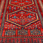 Full view red Persian-style rug with blue and orange medallion, patterned border, fringe.