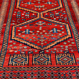 Full view red Persian-style rug with blue and orange medallion, patterned border, fringe.