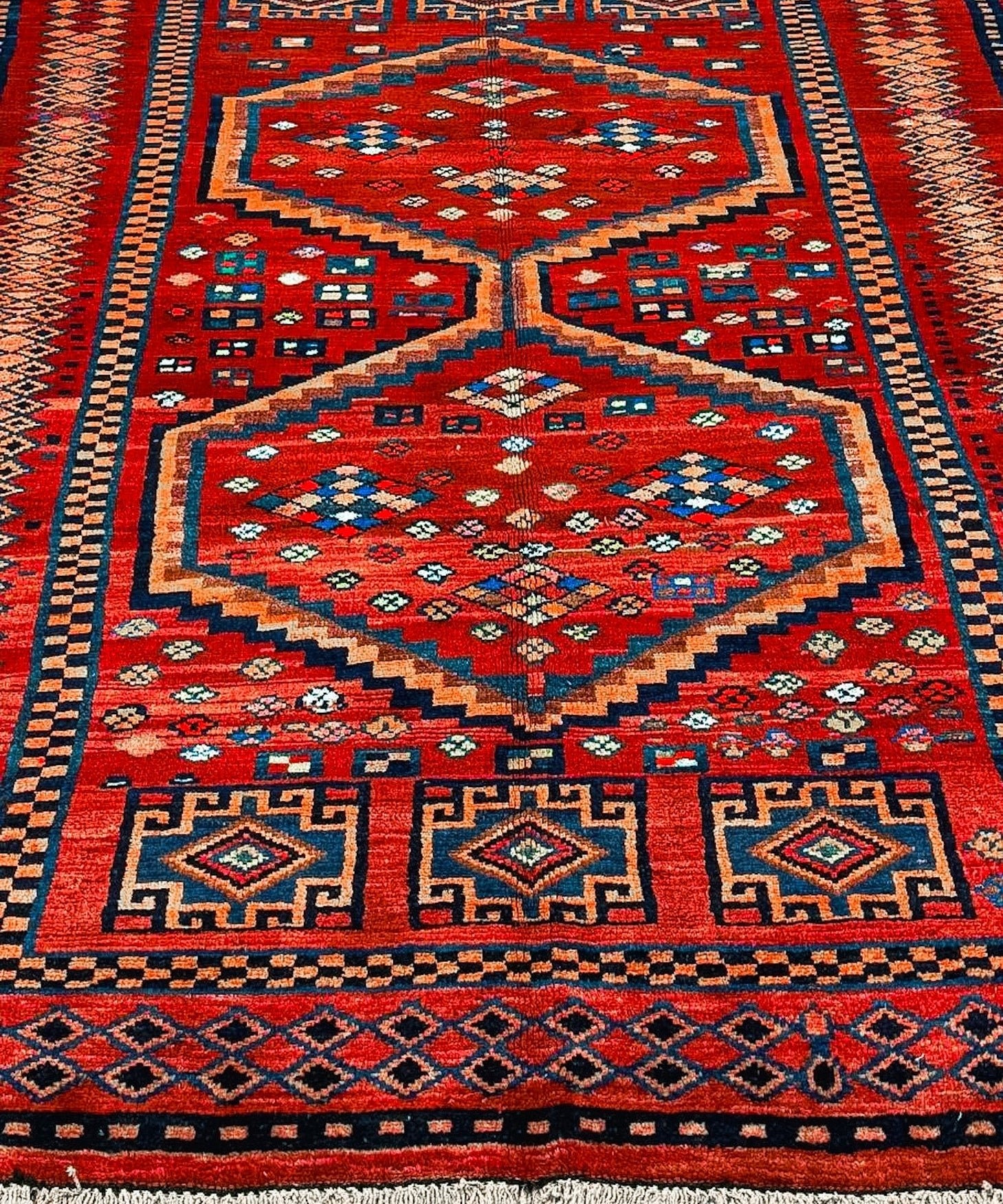 Full view red Persian-style rug with blue and orange medallion, patterned border, fringe.