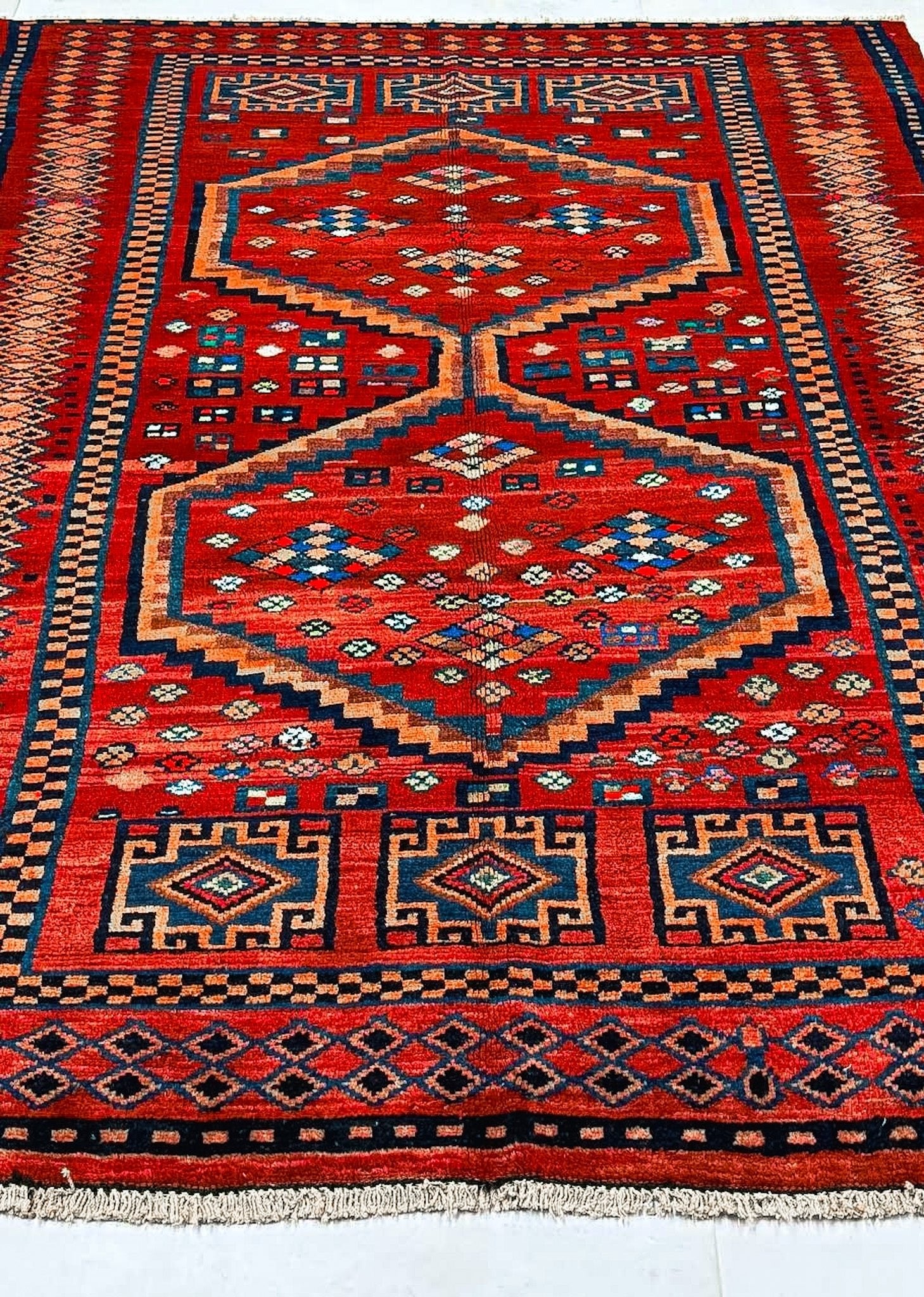 Full view red Persian-style rug with blue and orange medallion, patterned border, fringe.
