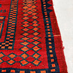 Red rug with navy and teal geometric motifs; orange accents; visible cream fringe at edge.