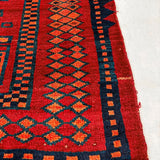 Red rug with navy and teal geometric motifs; orange accents; visible cream fringe at edge.