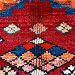 High-detail view of red rug center with blue, orange, white floral-like diamond motifs.