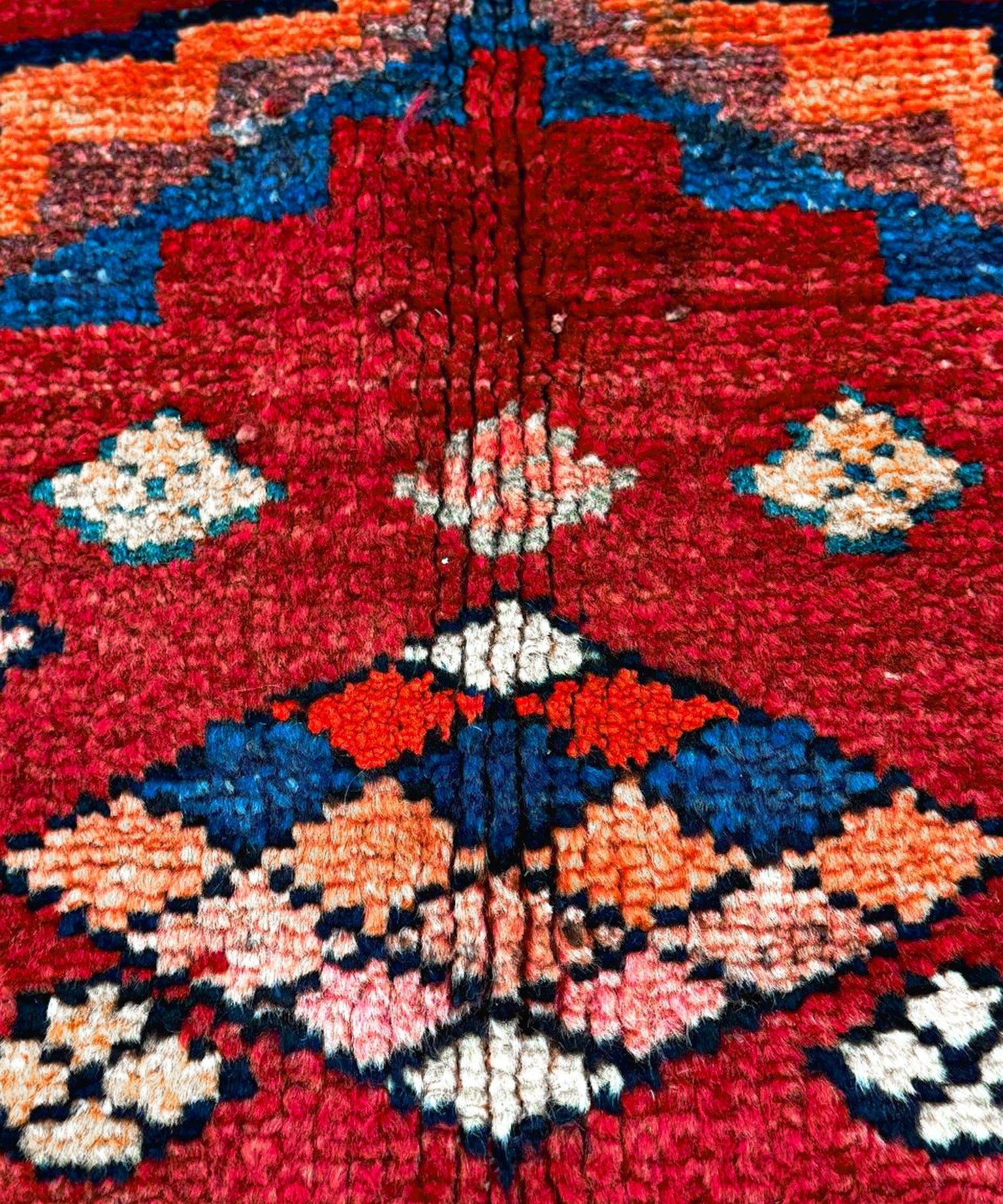 High-detail view of red rug center with blue, orange, white floral-like diamond motifs.