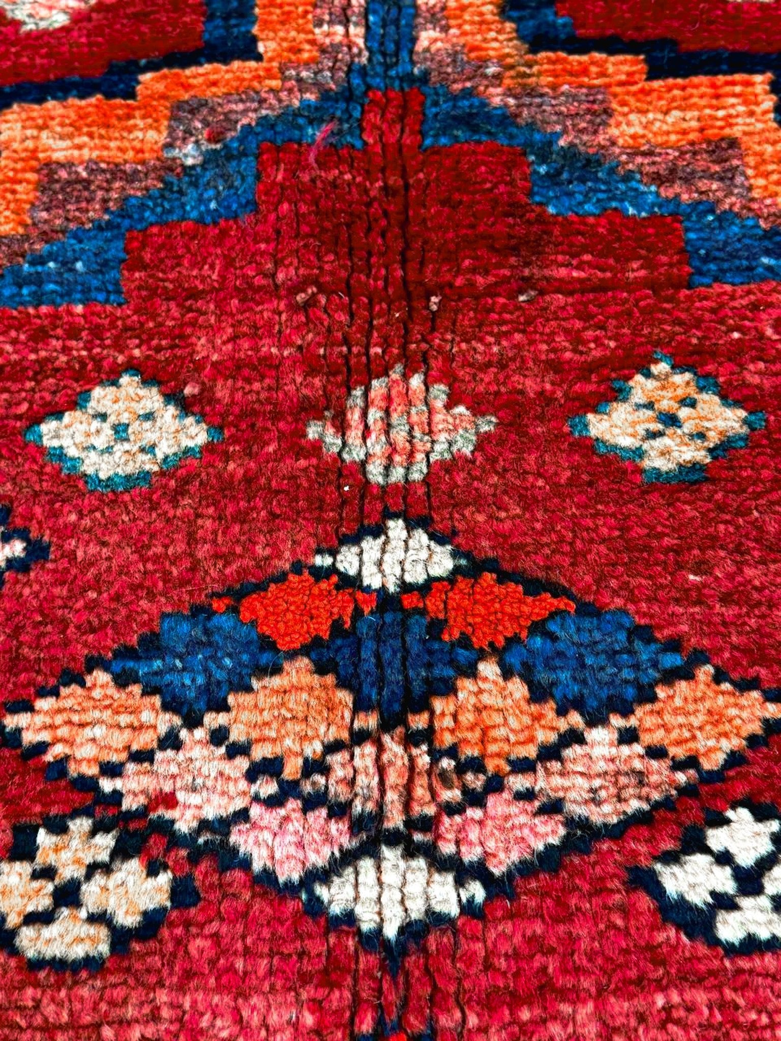 High-detail view of red rug center with blue, orange, white floral-like diamond motifs.