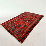 Red Persian-style area rug with navy and orange geometric medallion pattern, short fringe.