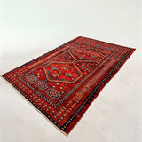 Red Persian-style area rug with navy and orange geometric medallion pattern, short fringe.