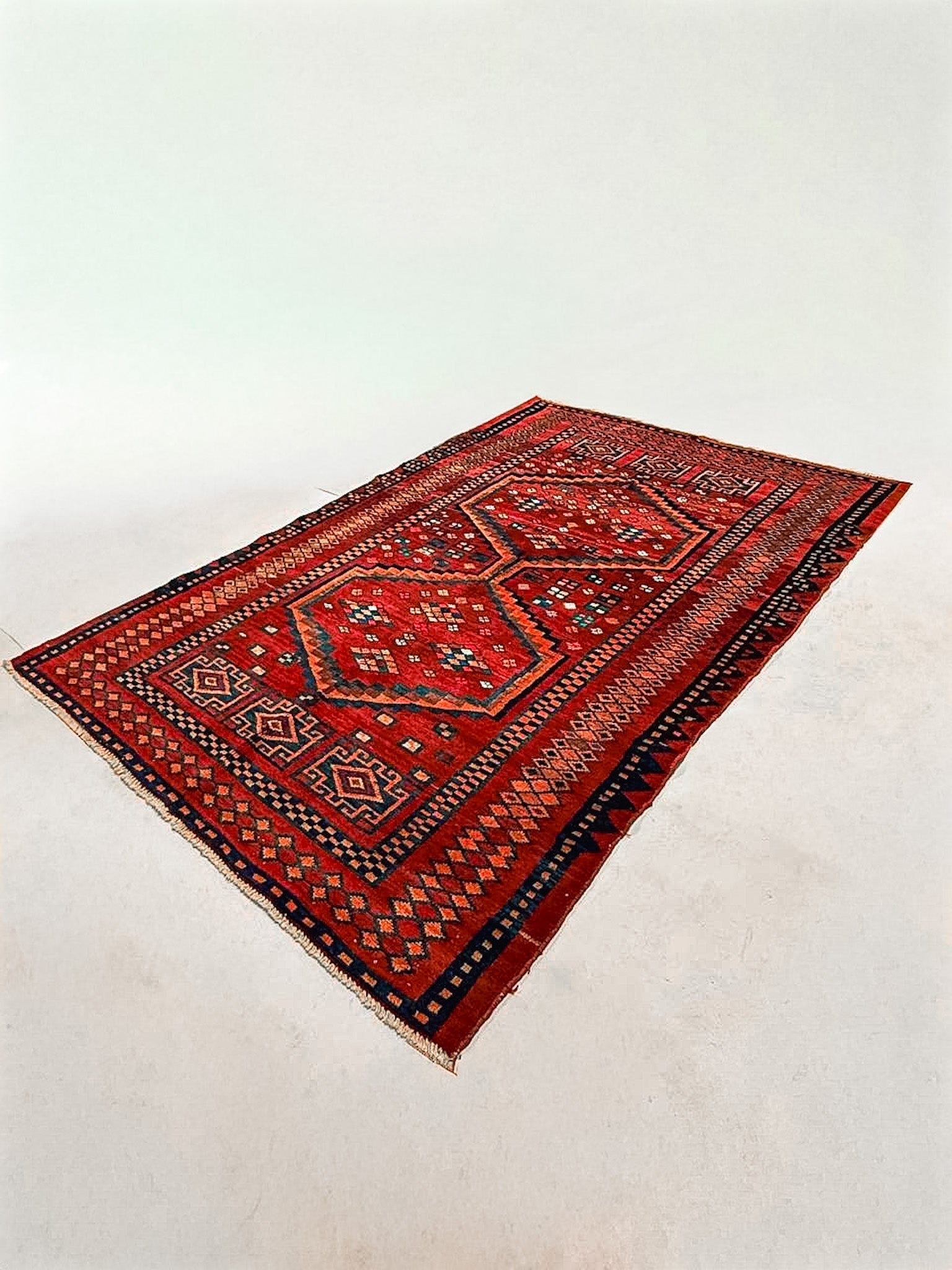 Red Persian-style area rug with navy and orange geometric medallion pattern, short fringe.