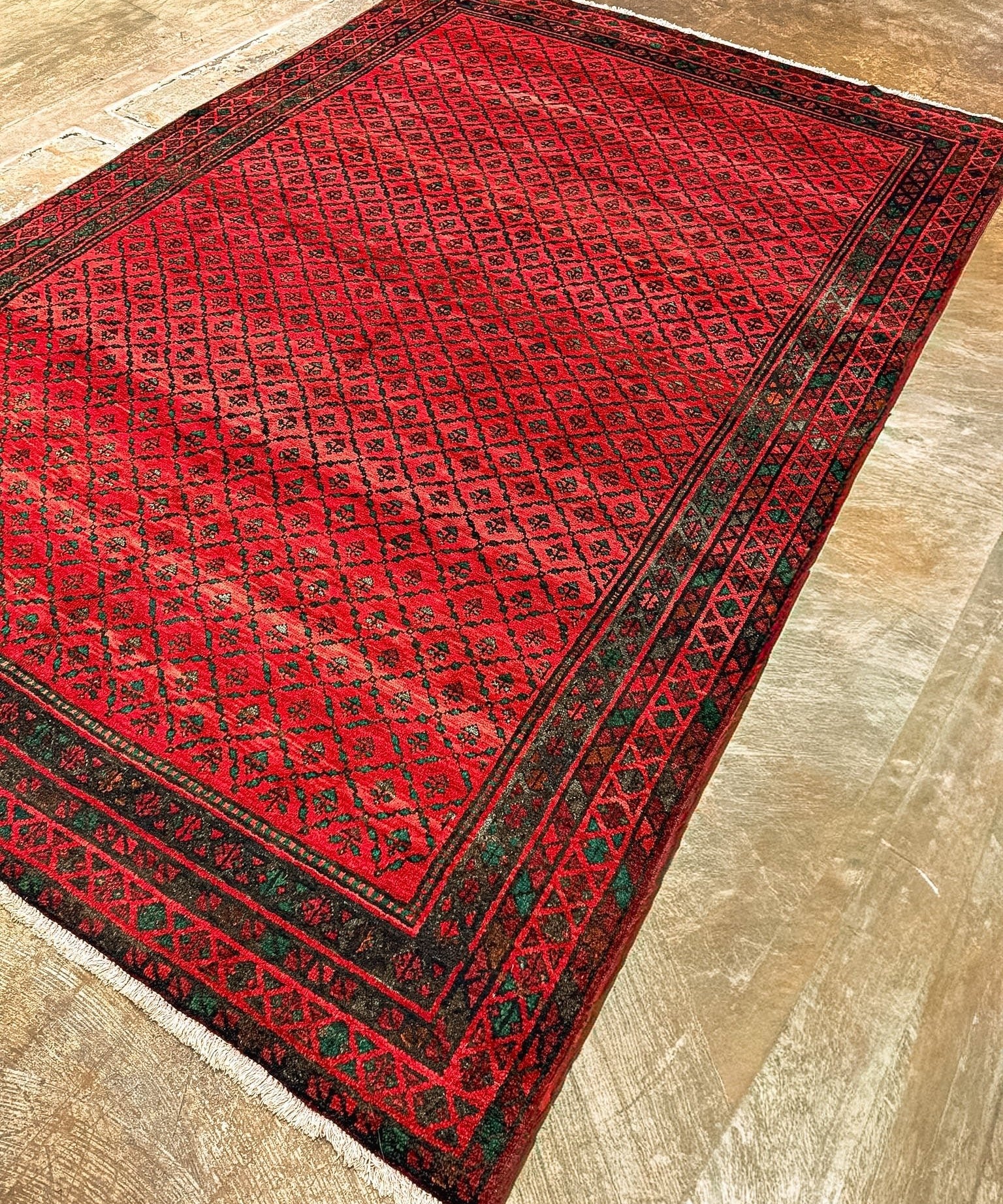Red area rug with diamond lattice design, dark edging, and short fringe corners.
