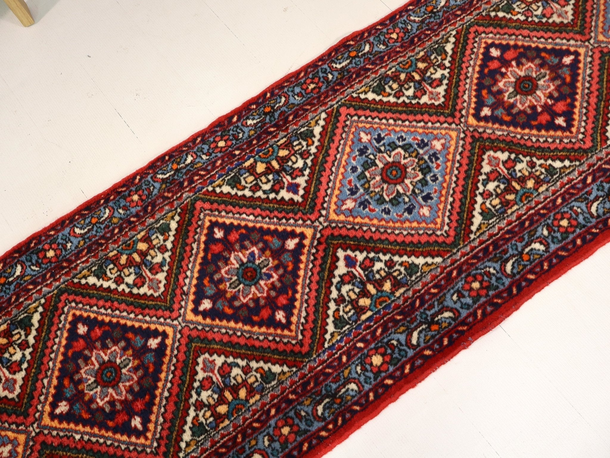 Persian runner rug corner section with repeating red, blue, and cream geometric motifs