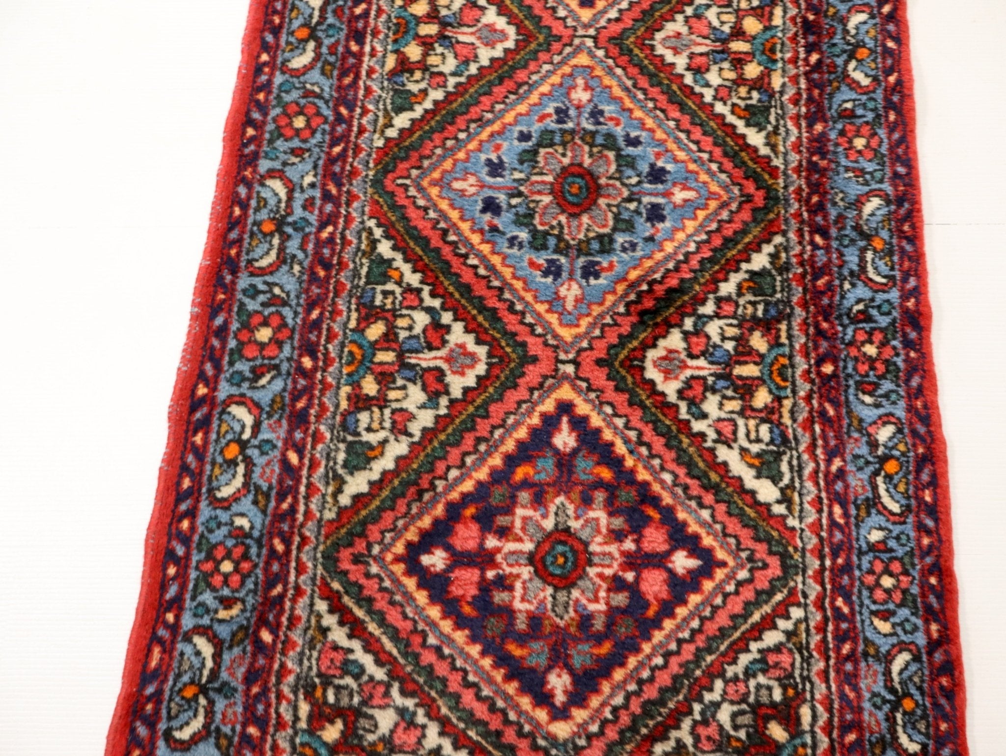 Persian runner rug close-up with large blue floral diamond and red geometric trim