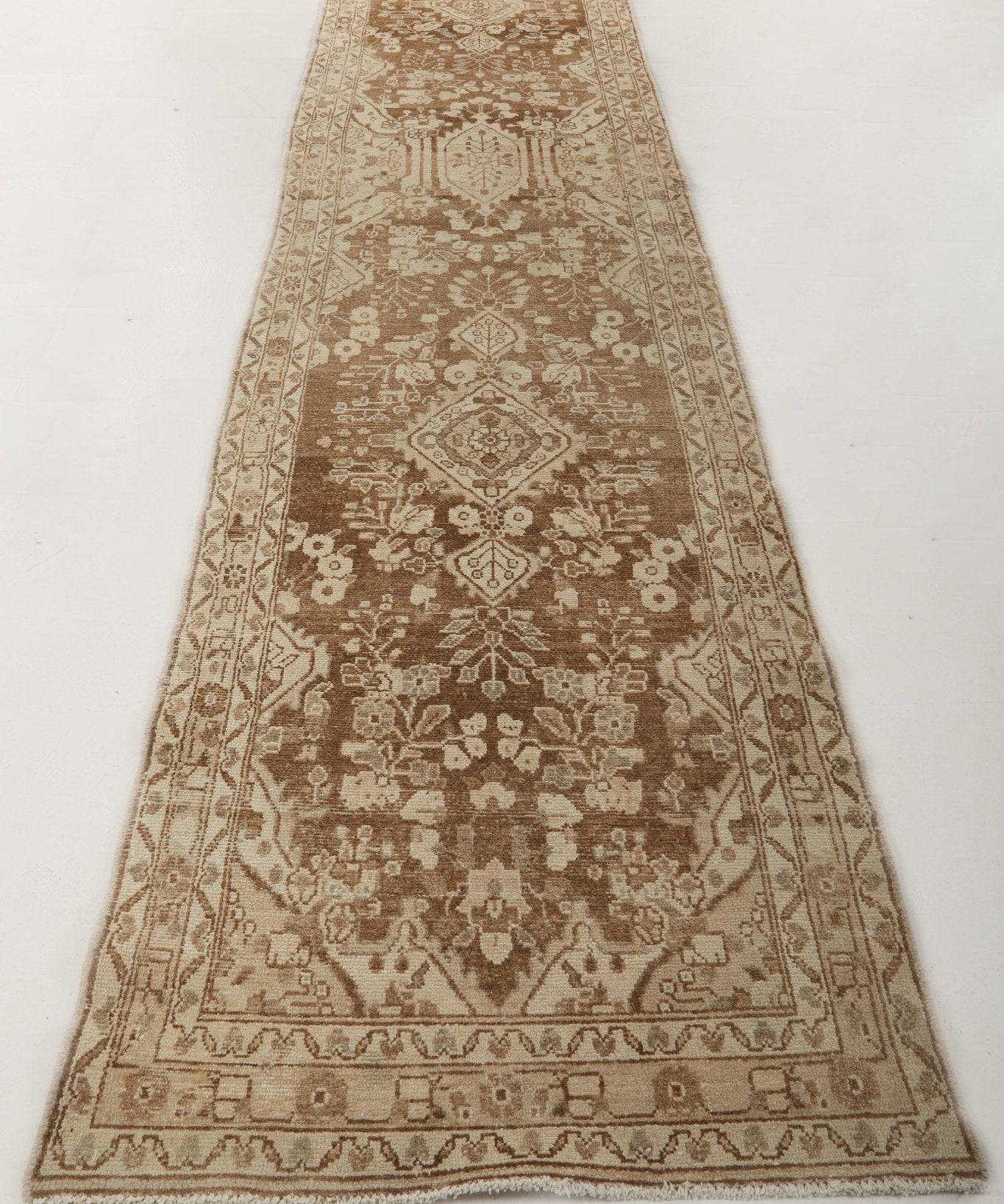 Runner rug with symmetrical center design, small floral motifs, and patterned border in brown
