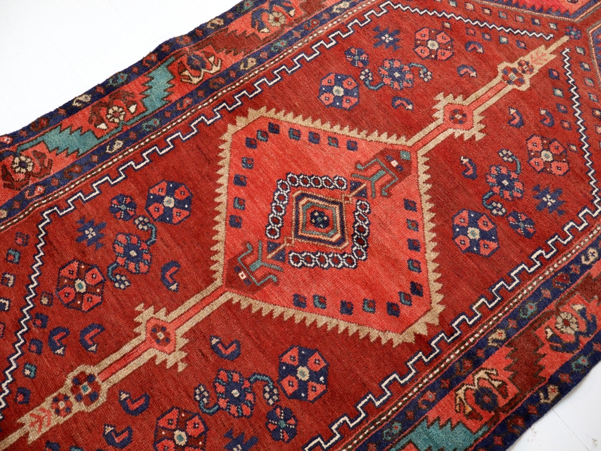 Persian Hamadan runner rug close-up: red field with navy motifs and cream border trim.