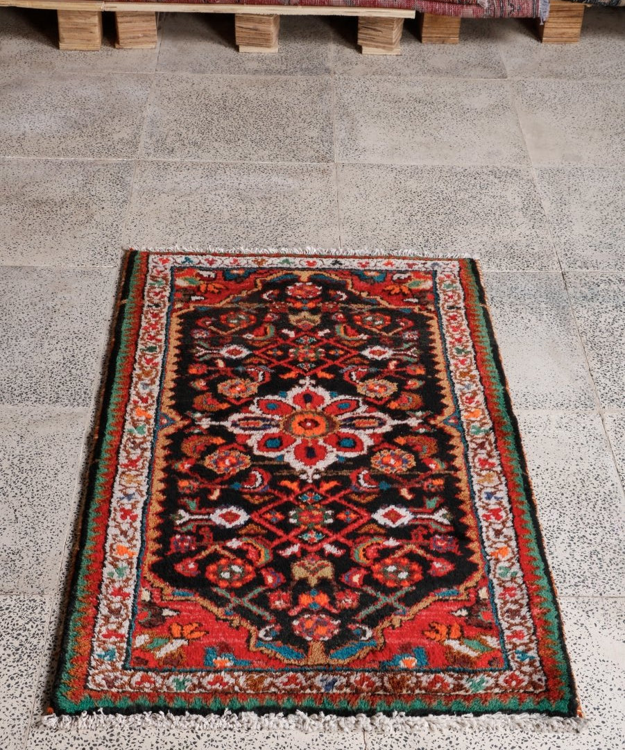 Black Persian-style rug with red and teal floral designs and detailed edge border