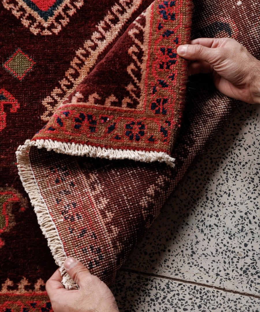 Rug corner detail with dark red field, multicolor border, and light fringe on edge