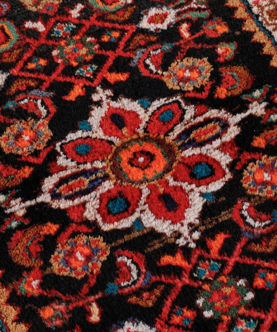 Close-up rug pattern: black background with red, teal, blue, and cream floral medallion motifs