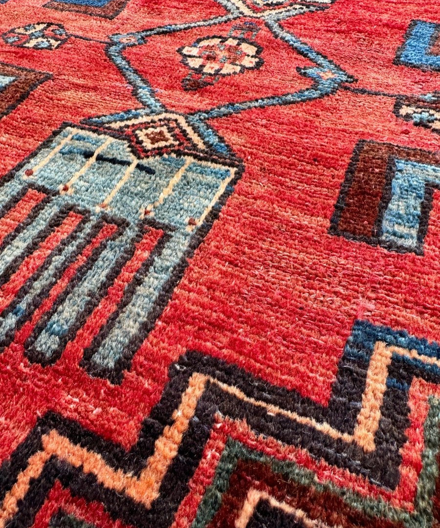 Persian-style rug close-up with red field and blue-gray geometric panels and dots