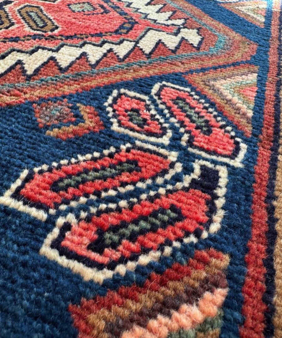 Close-up woven rug section with dark blue background, red accents, and patterned medallion.