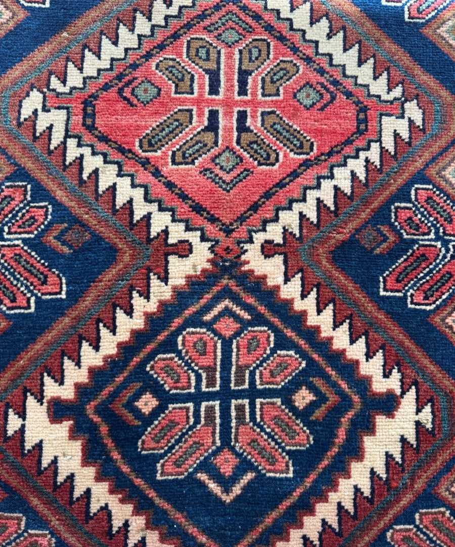 Close-up woven rug with red central medallion, blue fields, and zigzag geometric border.