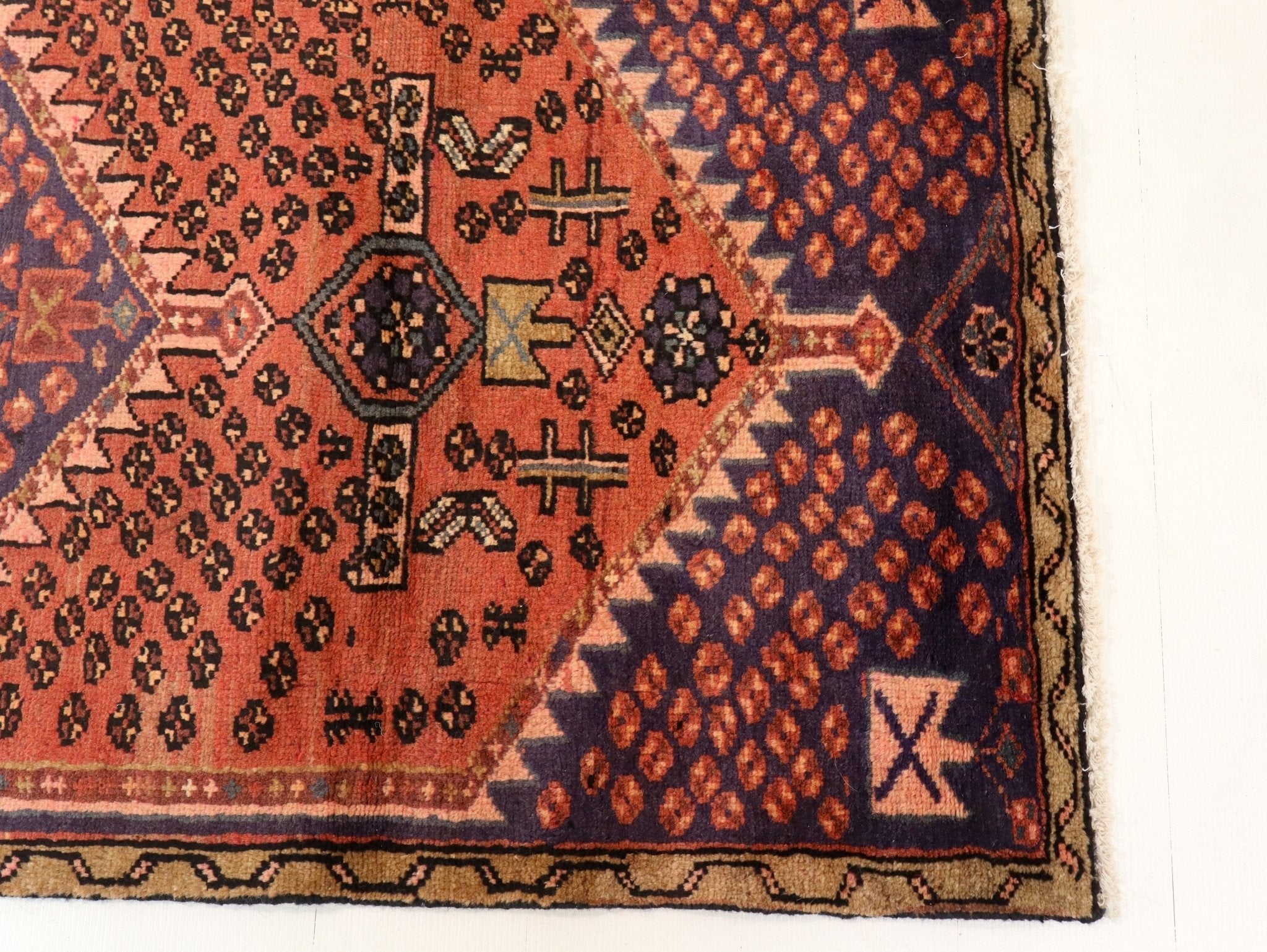 Persian Hamedan-style rug corner with rust red and navy geometric motifs and border