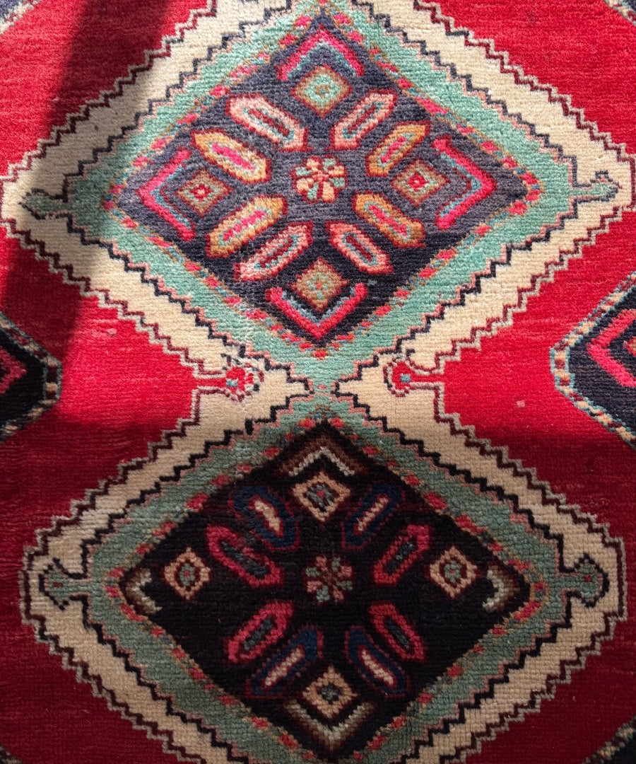 Persian Hamedan rug close-up with red background and stacked navy-and-cream square medallions