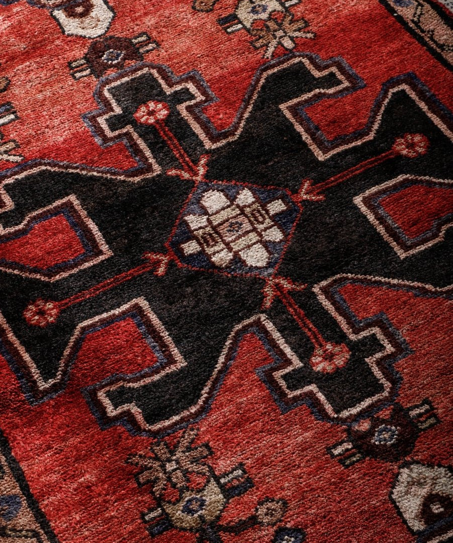 Close-up of red runner rug weave with black and beige geometric motifs.
