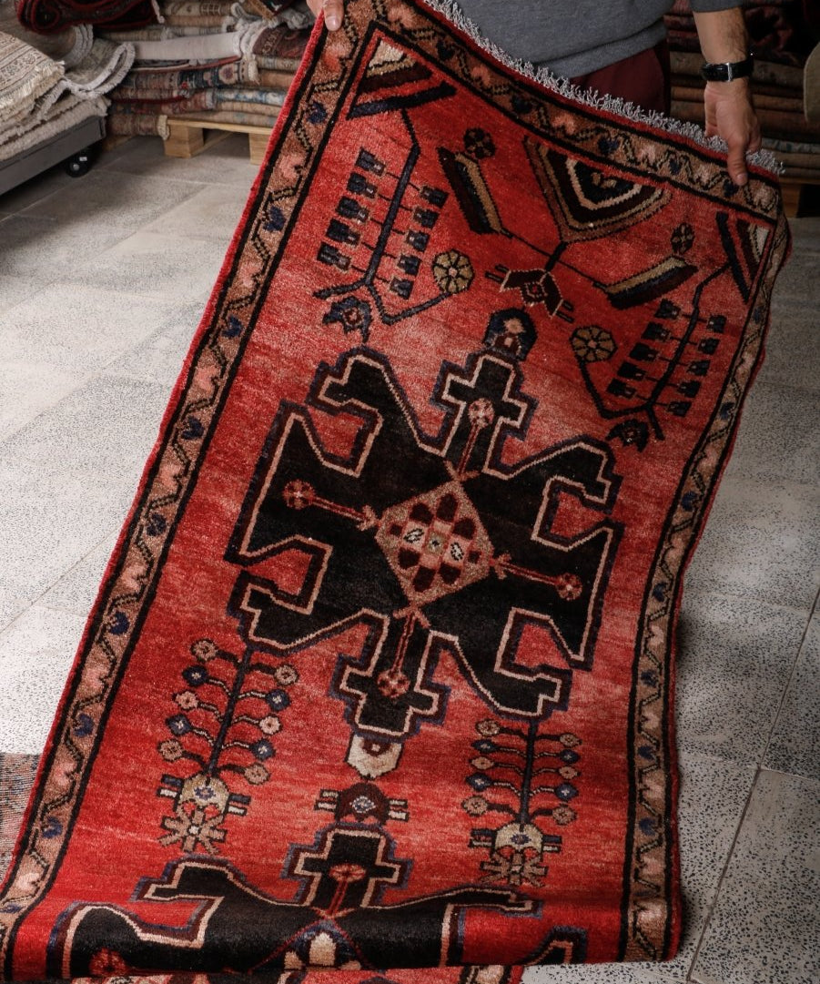 Red runner rug with black and beige motifs; held along the edge on the floor.