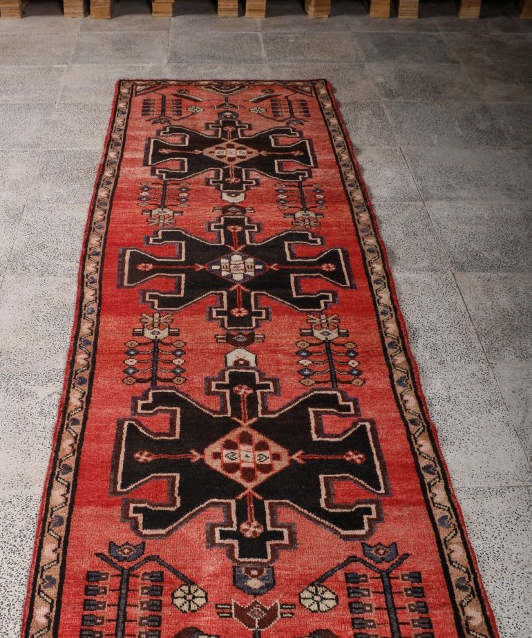Red runner rug with black cross-like shapes and beige pattern accents.