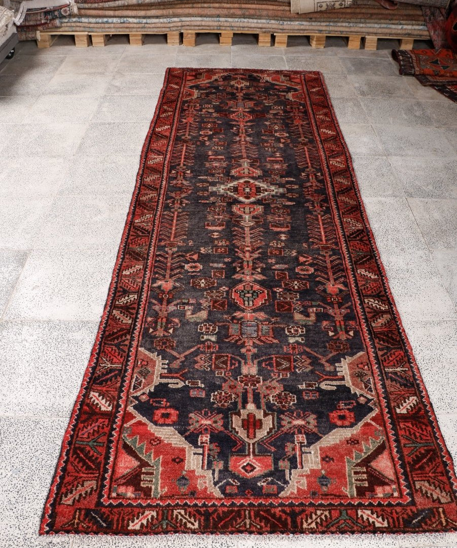 Persian Hamadan runner rug laid flat: dark navy center with red accents and repeating motifs