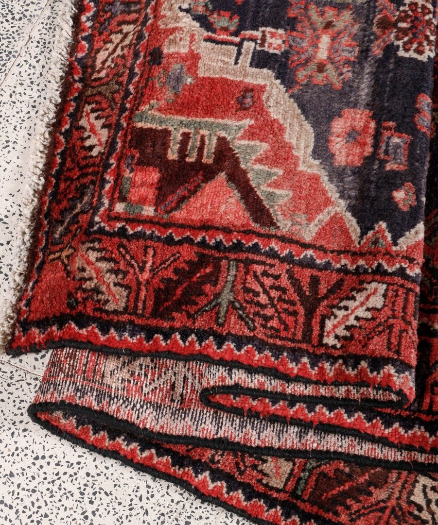 Persian Hamadan runner rug corner detail with red-and-cream patterning and dark border trim